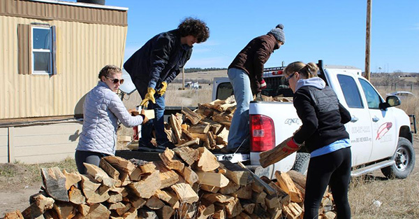 Four students loading cut firewood into the bed of a truck